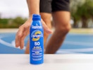 a hand reaching for a blue can of sunscreen spray