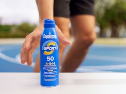 a hand reaching for a blue can of sunscreen spray