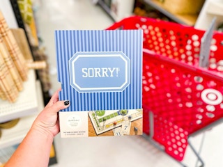 hand holding a magnolia sorry board game in front of a target cart