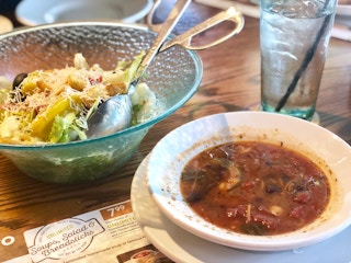 a bowl of soup near to a bowl of salad on a table with a menu on table