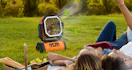 a portable orange fan next to a couple laying in the grass