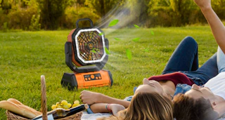 a portable orange fan next to a couple laying in the grass