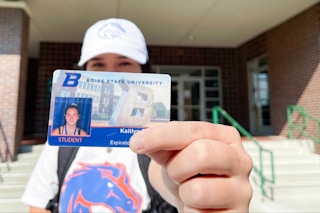 A college student holding out their student ID in front of an on-campus library