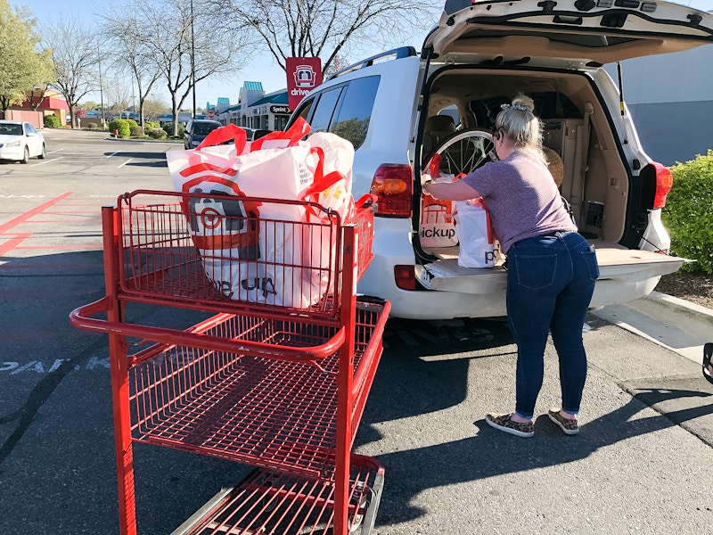 A person loading bags of groceries into the trunk of a vehicle next to a Target shopping cart.