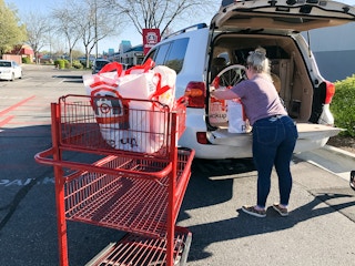 A person loading bags of groceries into the trunk of a vehicle next to a Target shopping cart.