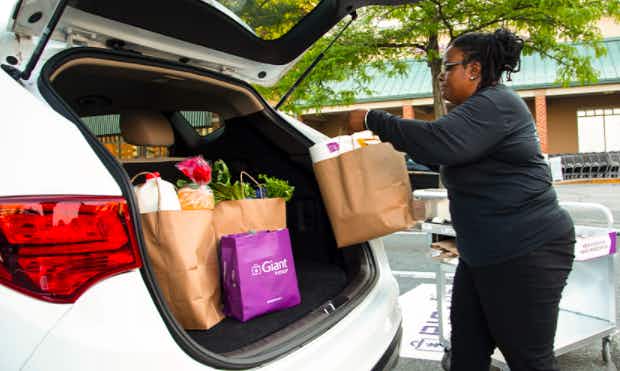 grocery store worker placing grocery bags in the trunk of a car
