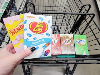 hand holding packets of starburst & jelly belly drink mixes over a cart with more drink mixes