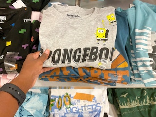 someone picking up a shirt on a display of other t-shirts