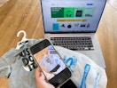 A person holding a cell phone, with a photo of a kids Nike outfit on it, next to a computer with Ebay up on the computer screen.