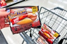 person holding ball park franks over a cart with another pack of ball park franks in it