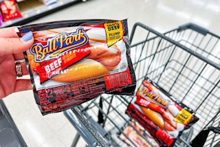 person holding ball park franks over a cart with another pack of ball park franks in it