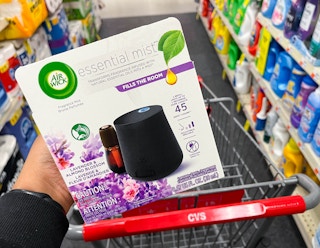 person holding up Air Wick Essential Mist diffuser in front of cart