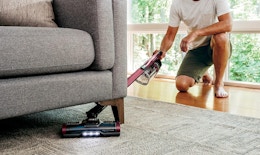 a person vacuuming under a couch 
