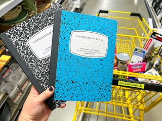 Someone holding up two composition notebooks next to a cart at Dollar General