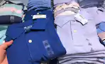A person's hand taking a children's school uniform polo shirt from a table at The Children's Place.