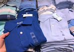 A person's hand taking a children's school uniform polo shirt from a table at The Children's Place.