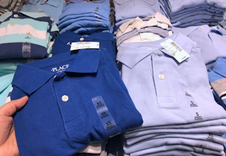 A person's hand taking a children's school uniform polo shirt from a table at The Children's Place.