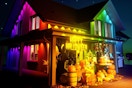 The outside of a house lit in rainbow colors around the eaves with a Halloween display in front of it.