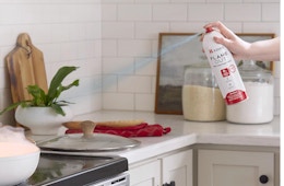 a hand spraying fire extinguishing spray at a pan on a stove