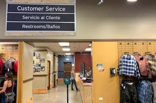 Person standing at REI customer service counter with clothing displays in front