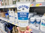 Gold Bond Healing Hand Cream held out in front of a shelf full of other lotions.