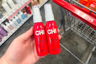 person holding 2 chi heat protection sprays by a cart
