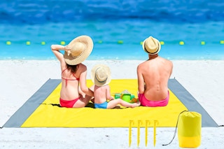 Lifestyle image of large yellow beach blanket on the beach used by a family of three