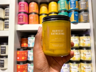 a person holding a fall scented candles with a display of candles behind in bath and body works