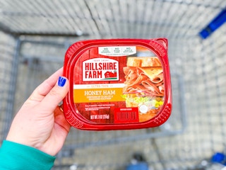 hand holding a tub of hillshire farm deli meat over walmart cart