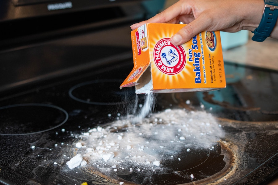 A person sprinkling baking soda onto a stove