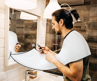 a man shaving over a beard bib over a bathroom sink
