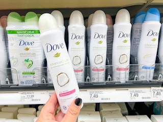 Hand holding Dove dry spray in front of a shelf with other Dove dry sprays