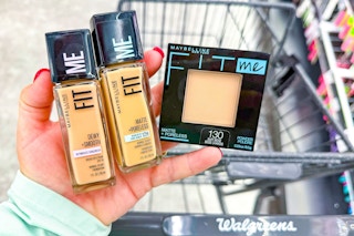 hand holding maybelline fitme foundation and powder next to a walgreens shopping cart