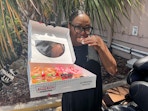 A woman eating a Mother's Day doughnut from Krispy Kreme, holding up a box of more doughnuts