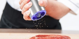 A person using a salt and pepper shaker on a steak