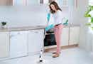 person with cleaning gloves on in the kitchen using cordless scrubber to clean floor