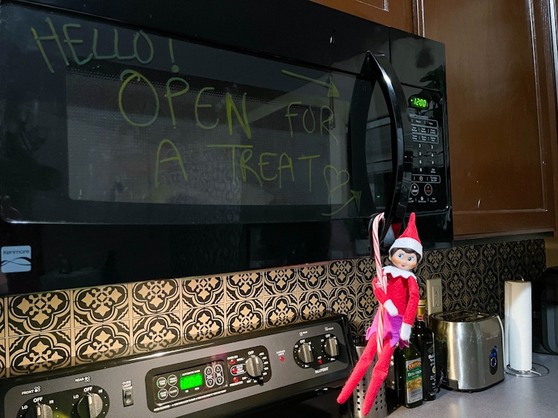 elf on the shelf hanging on the microwave with candy canes