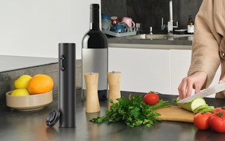 an electric wine opener on a counter next to a person cutting up veggies