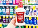 person holding a bottle of colgate mouthwash in front of shelves of mouthwash