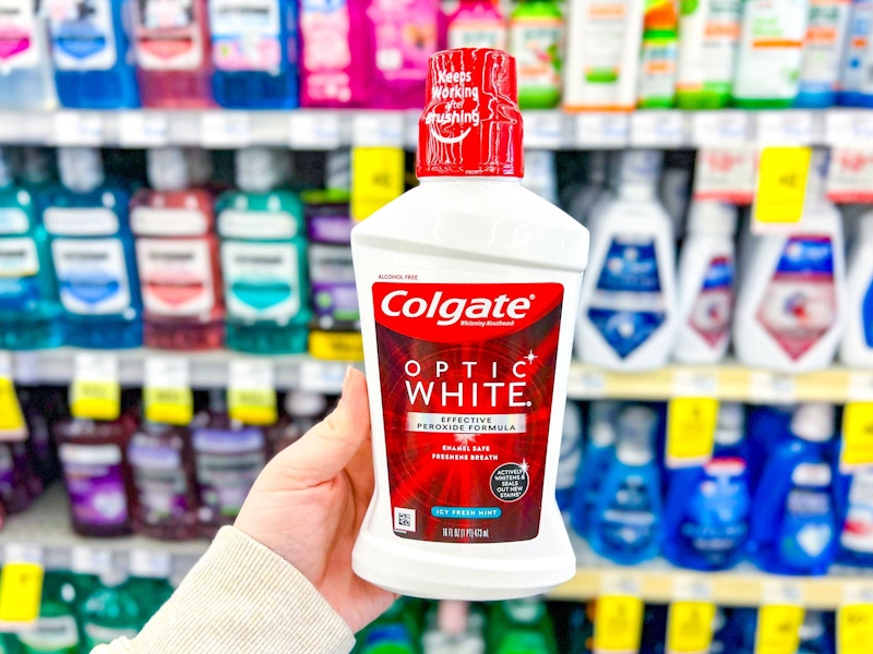 person holding a bottle of colgate mouthwash in front of shelves of mouthwash