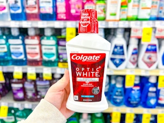 person holding a bottle of colgate mouthwash in front of shelves of mouthwash