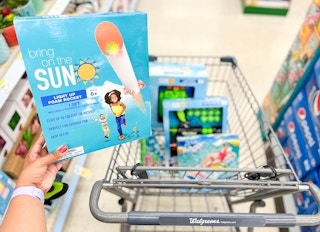 hand holding up box of light up foam rockets in front of various summer items inside cart in background