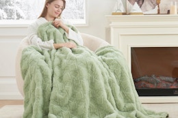 Woman using the Cozy Bliss Faux Fur Textured Throw Blanket sitting on a chair.