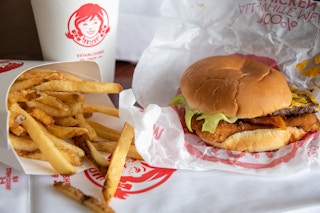 Wendy's fries, a drink, and a chicken, beef, bacon burger sitting on a table at Wendy's..
