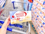 hand holding premier protein shakes over shopping cart