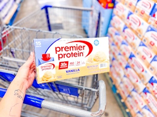 hand holding premier protein shakes over shopping cart