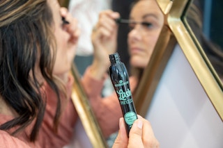 A woman applying Essence Lash Princess mascara in front of a mirror.