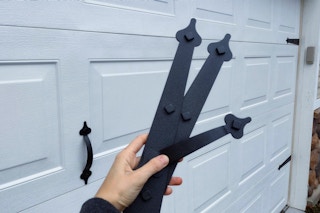 A person's hand holding up some magnetic decorative garage door hardware in front of a garage door.