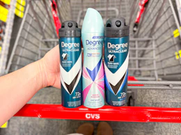 person holding 3 degree dry spray deodorants over a cart