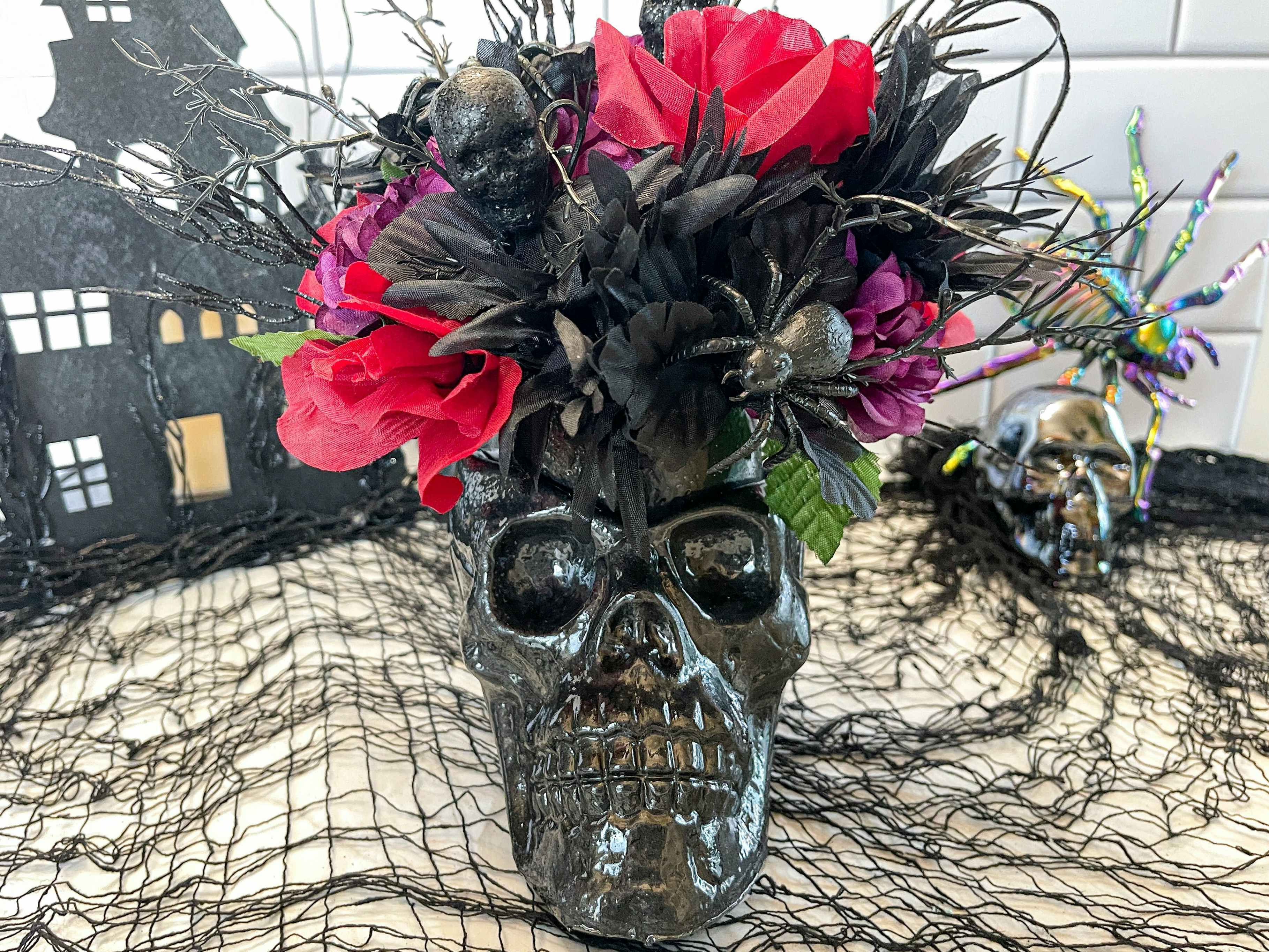 A black skull vase with black and red flowers inside sitting alongside other Halloween decor.